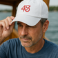 Man wearing a white cap with red 4547 logo by a body of water